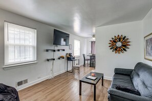 Ein Wohnzimmer mit grauem Sofa, einem Couchtisch, einem an der Wand montierten Fernseher und einem dekorativen Wandkunstwerk in Sonnenform.