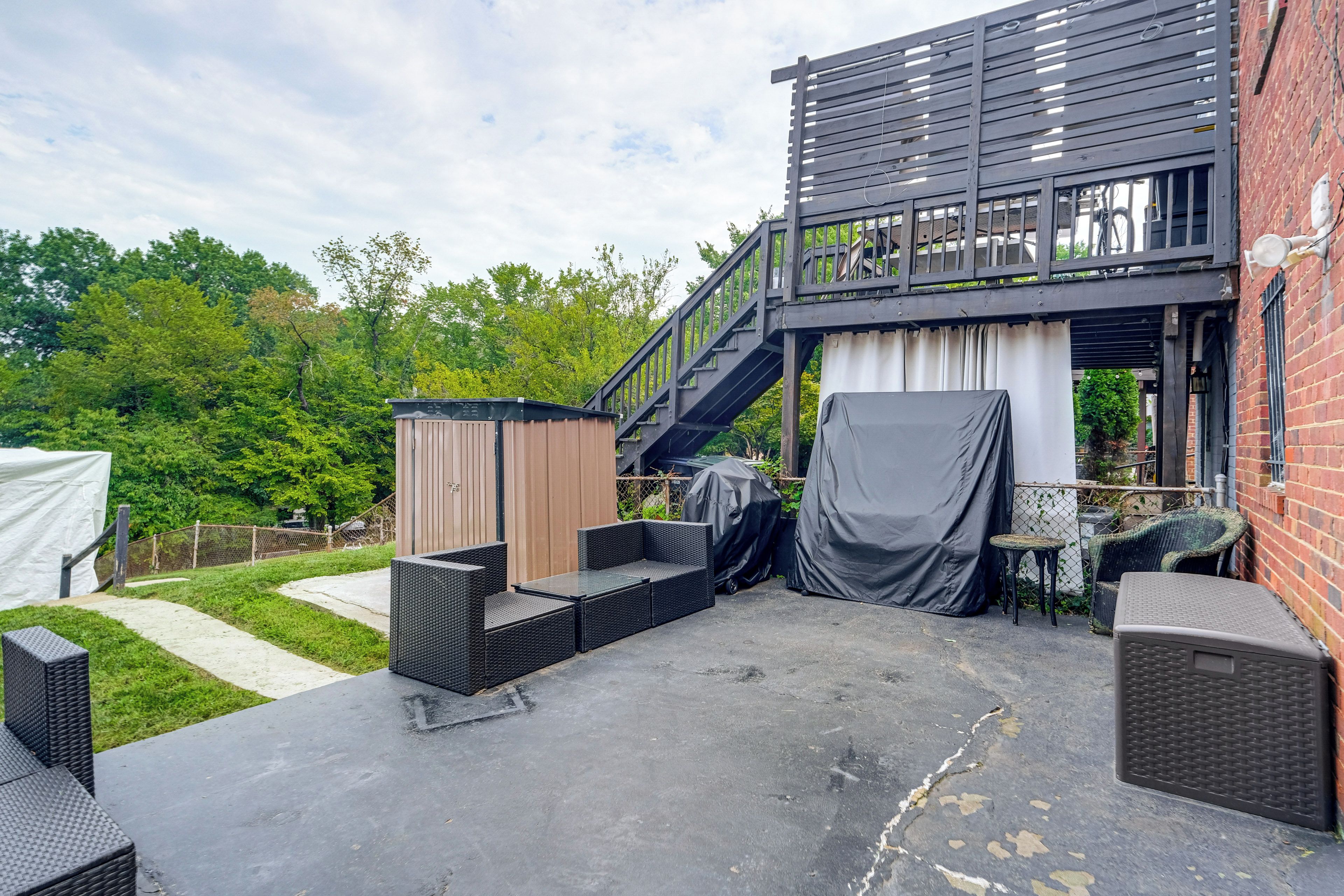 An outdoor patio area with a covered seating area, a barbecue grill, and a staircase leading to an upper level.