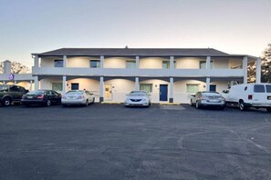 A motel with a two-story structure, a parking lot with several cars, and a clear sky.