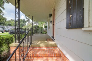 A covered porch with a brick step leading to a door, a metal railing, and a view of a green lawn and parked cars. - 2 Mi to Augusta National: Walkable Neighborhood! (Augusta)