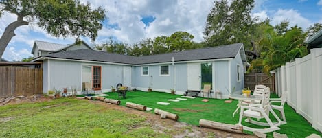 A residential backyard with a lawn, a wooden deck, and a white house with a grey roof.