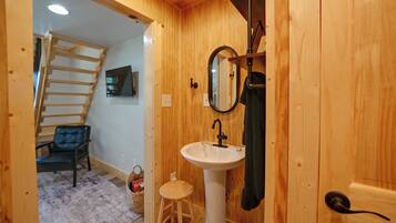 Un interior de madera con un lavabo blanco, un espejo, una toalla, un taburete y una silla.
