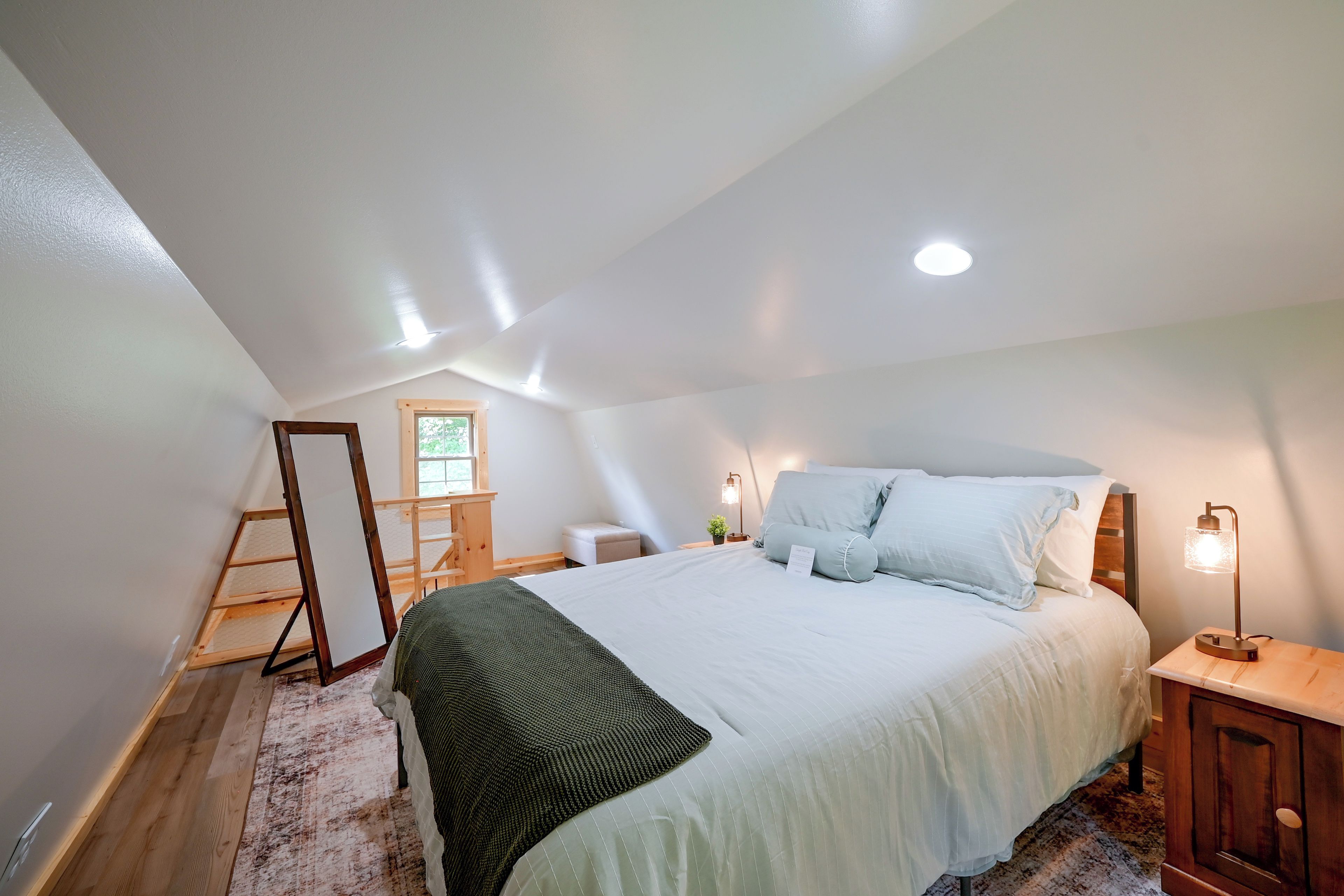 Un dormitorio con una cama grande, una escalera de madera, una mesita con una lámpara y una ventana.