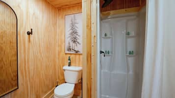 A wooden interior with a toilet, a shower, and a shelf with toiletries.