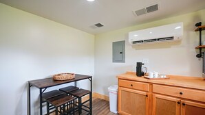 A compact kitchen with a wooden table, a coffee maker, and a trash bin.
