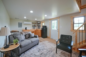 A compact living space with a kitchenette, a sofa, a chair, and a small table with a lamp.