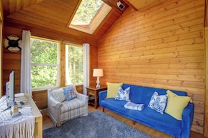 A cozy cabin interior with a blue sofa, striped armchair, and a small table with a lamp. - Walk to Beach! Kitsap Coast Retreat w/ Hot Tub (Hansville)