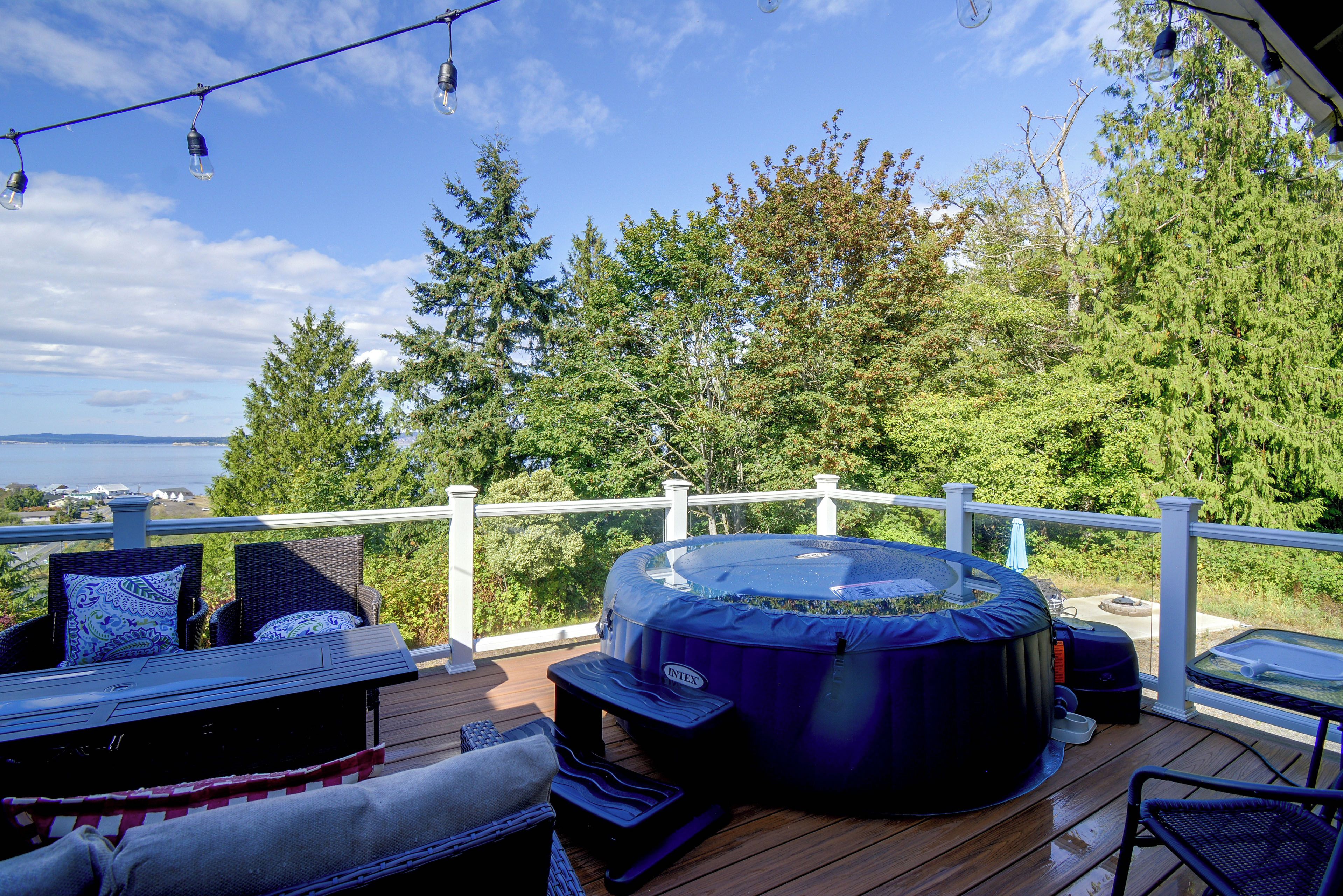 En terrasse med jacuzzi, havemøbler og udsigt til træer og havet.