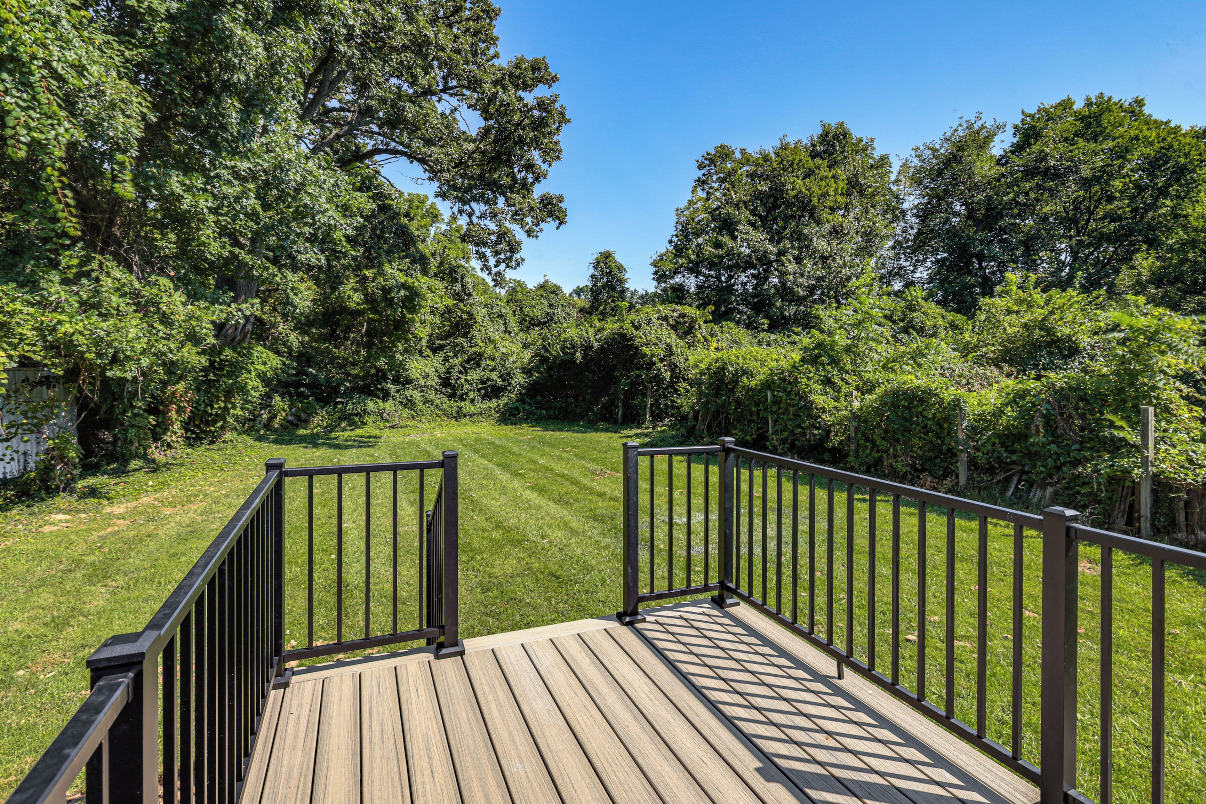 A wooden deck with metal railings, surrounded by lush greenery and trees.