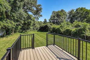 A wooden deck with metal railings, surrounded by lush greenery and trees.