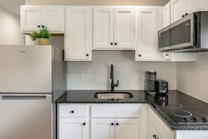 A kitchen with white cabinets, a stainless steel refrigerator, a black microwave, a coffee maker, and a gas stove.