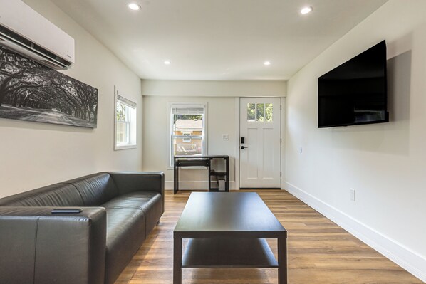 A modern living room with a black leather sofa, a dark wooden coffee table, and a flat-screen TV mounted on the wall.