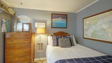 A bedroom with a wooden dresser, a bed with a blue quilt, a map on the wall, and a framed picture of a sailing event.