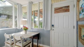 A room with a white door, a table with chairs, a vase with flowers, and a window with curtains.