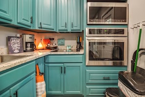Una cocina con gabinetes color turquesa, una cafetera, una estufa y un microondas.