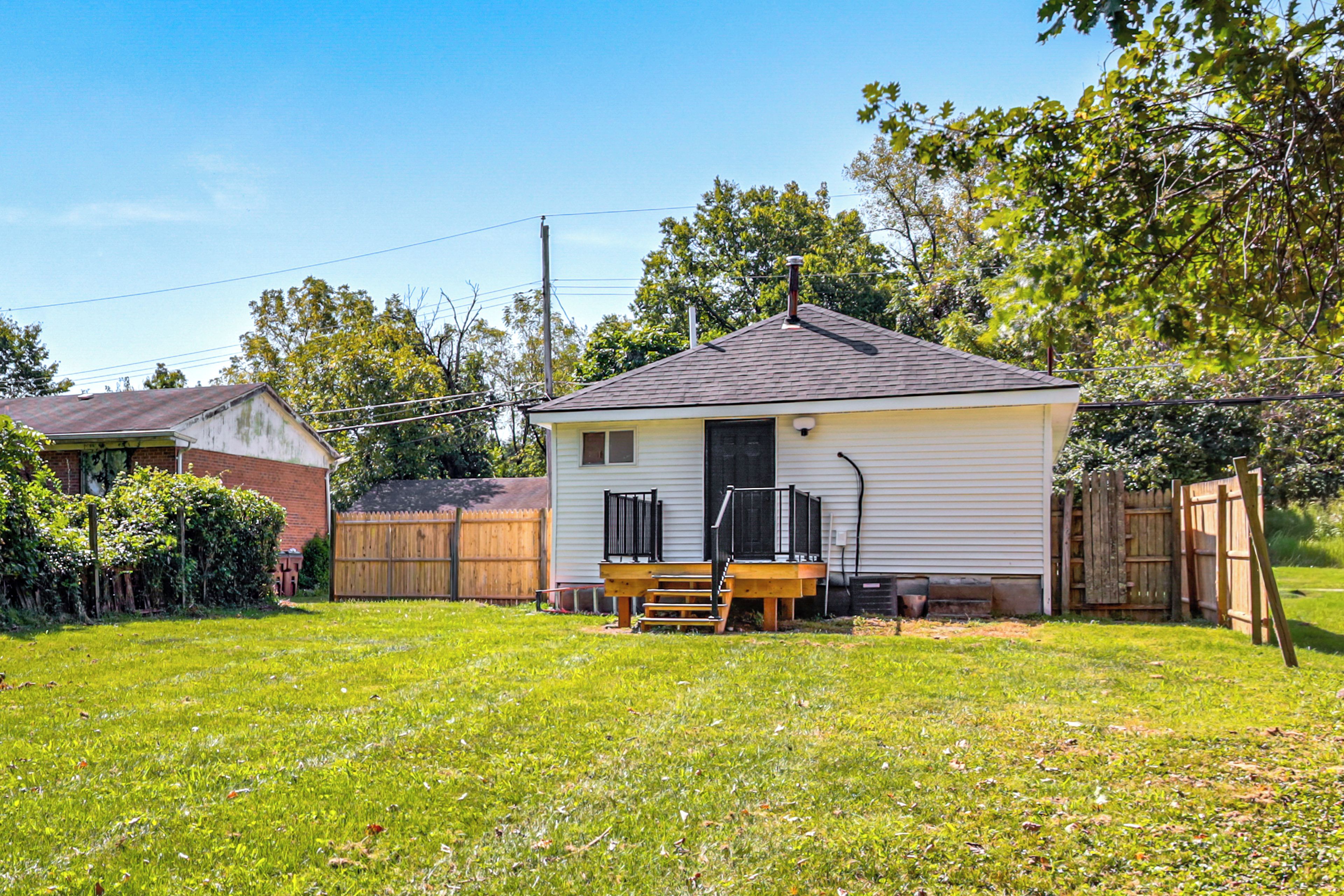 A small single-story house with a front porch, a wooden deck, and a fenced backyard.