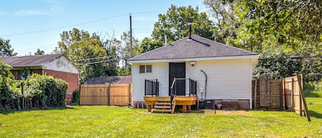 A small single-story house with a front porch, a wooden deck, and a fenced backyard.