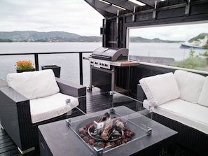 An outdoor deck with wicker furniture, a grill, and a glass table with wood burning.
