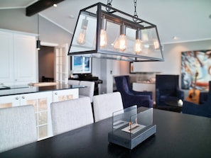 A modern dining area with a glass-top table, metal pendant light fixture, and a clear glass candle holder.