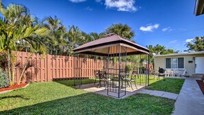 Ein Garten mit überdachter Terrasse, Holzzaun und Rasen.