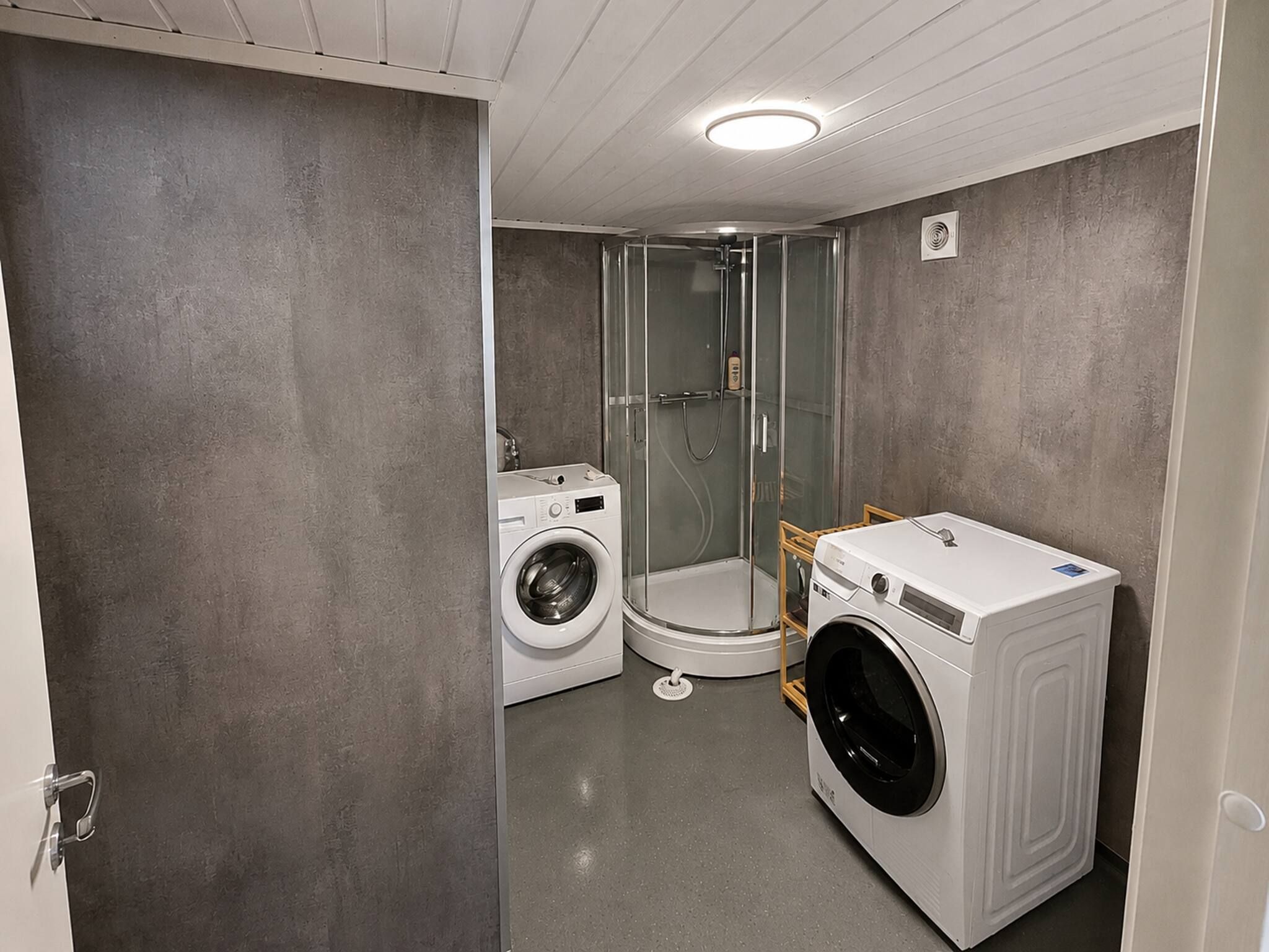 Et lille badeværelse med vaskemaskine, brusekabine og toilet.