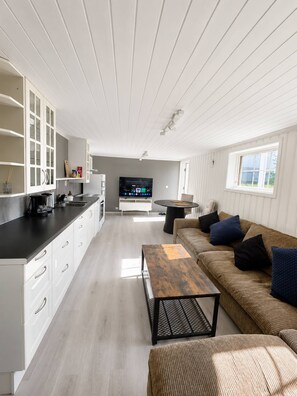 A modern kitchen with white cabinetry, a black countertop, and a built-in TV. There is a dining area with a round table and a sofa with cushions. - Bright & Spacious Guest Suite Near Drammen (Drammen)