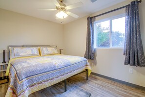 Ein Schlafzimmer mit einem Bett, einem Deckenventilator, einem Fenster mit Vorhängen und einem Nachttisch.