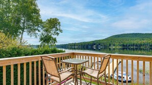 A wooden deck with a glass table and chairs overlooking a calm lake and forested hills. - On Neal Pond! Spacious Group Retreat w/ Game Room (Lunenburg)