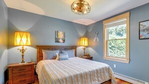 A bedroom with a bed, two bedside tables with lamps, a window, and a painting on the wall. - On Neal Pond! Spacious Group Retreat w/ Game Room (Lunenburg)