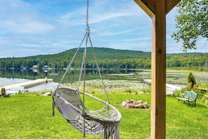 A hammock hanging from a wooden structure overlooking a lake with a forested hill in the background. - On Neal Pond! Spacious Group Retreat w/ Game Room (Lunenburg)