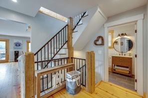 A staircase with wooden railings and a letter 'R' decoration, leading to a room with a wooden floor and a bathroom with a mirror and sink. - On Neal Pond! Spacious Group Retreat w/ Game Room (Lunenburg)
