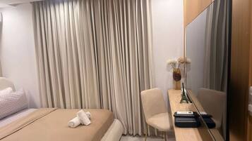 Habitación de hotel con una cama, un escritorio con televisor de pantalla plana, una silla y un jarrón con flores.