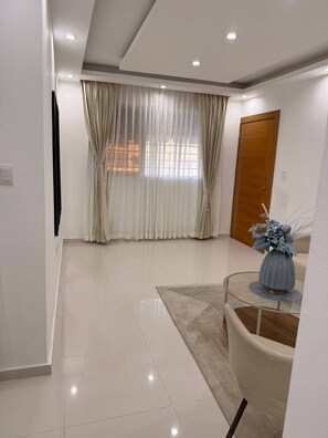 A modern living room with a glass coffee table, a wooden door, and a large window with curtains. - Nice apartment close to everything (Santo Domingo Norte)