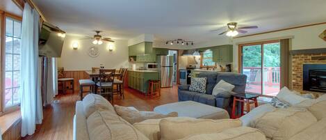 A spacious living room with a large sofa, a dining area with wooden chairs, a kitchen with green cabinets, and a fireplace.