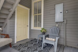 A room with a grey door, a window with blinds, a grey chair, a small table with a plant, and a grey utility box. - Historic Jacksonville Home: Near EverBank Stadium (Jacksonville)