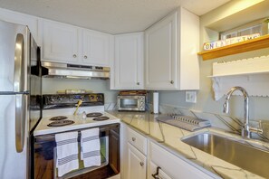 Cozinha moderna com eletrodomésticos de aço inoxidável, armários brancos e bancada de mármore.