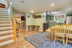A spacious kitchen with green cabinets, a dining area with a patterned rug, and a wooden staircase.