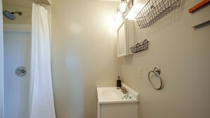 A bathroom with a shower, a sink, a mirror, and a towel rack.