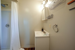 Un baño con ducha, lavabo, espejo y toallero.