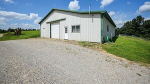 A single-story building with a white exterior and green roof, a gravel driveway, and a grassy area with trees in the background.