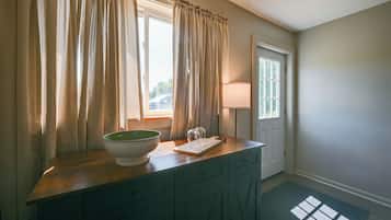 A bathroom with a wooden vanity, a bowl sink, a mirror, and a window with curtains.