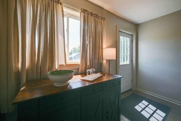 A bathroom with a wooden vanity, a bowl sink, a mirror, and a window with curtains.