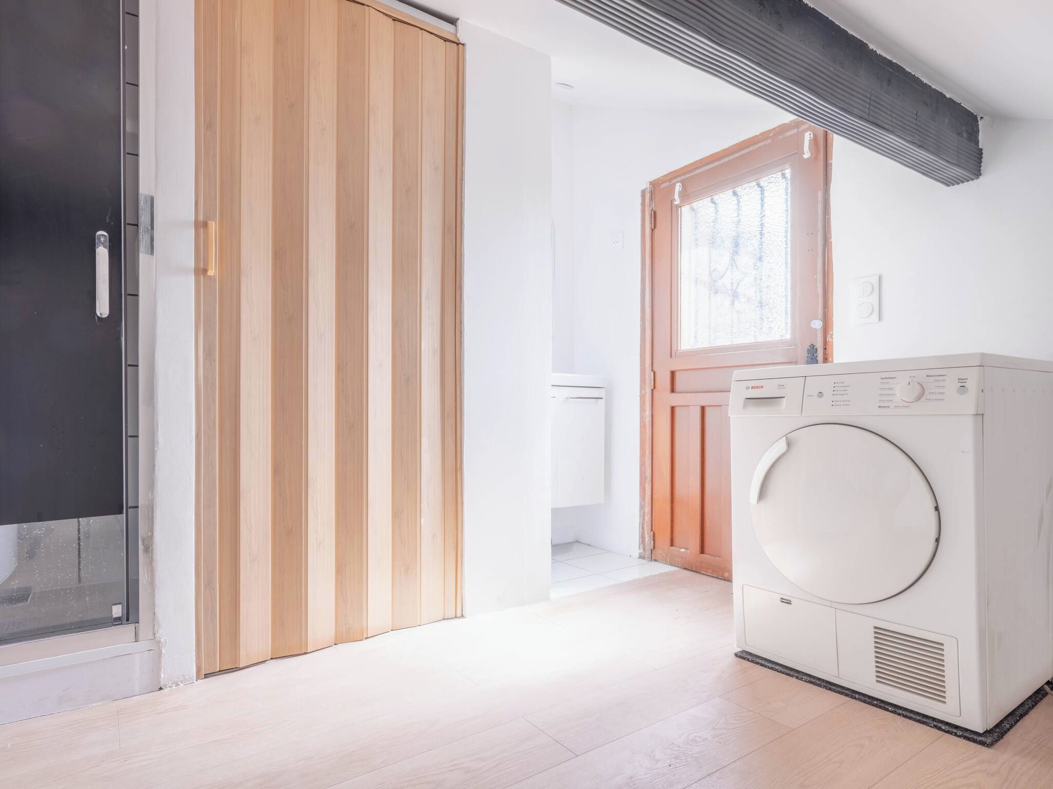 Une buanderie avec un lave-linge blanc, une porte en bois et une fenêtre.