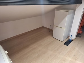 A room with a white refrigerator, wooden flooring, and a power outlet on the wall. - Renovated studio in the attic — Paris 30 minutes away (Argenteuil)