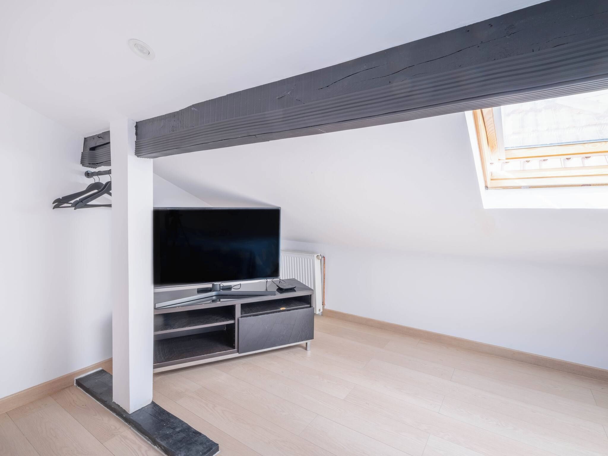 A room with a TV on a stand, a radiator, and a window with blinds.