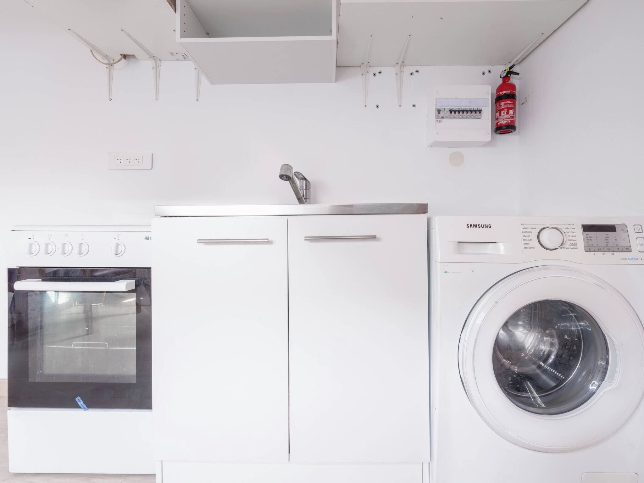 A kitchen with a dishwasher, a washing machine, and a fire extinguisher.