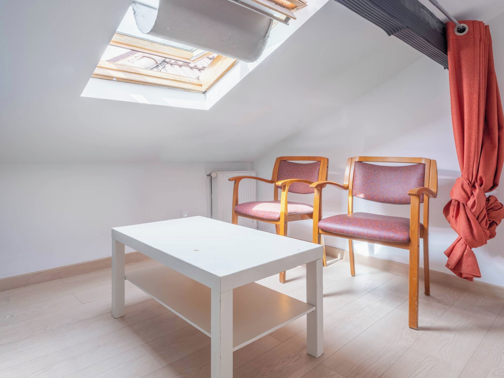 Une petite pièce lumineuse, dotée d’une lucarne, de deux chaises en bois à assise rembourrée et d’une table blanche.