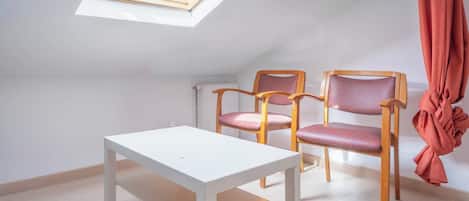 Une petite pièce lumineuse, dotée d’une lucarne, de deux chaises en bois à assise rembourrée et d’une table blanche.