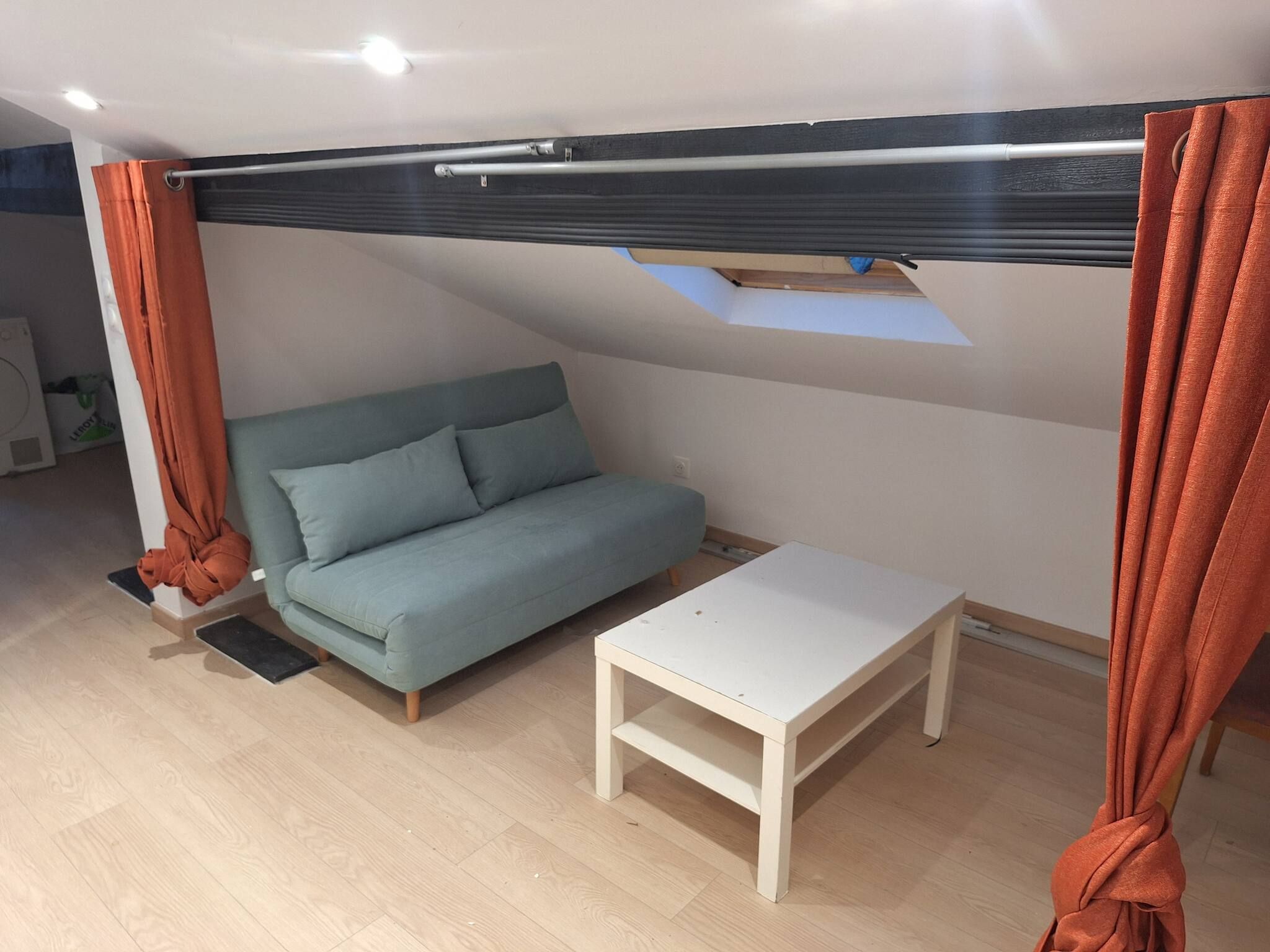 A compact room with a sofa, a small table, and a window with curtains.