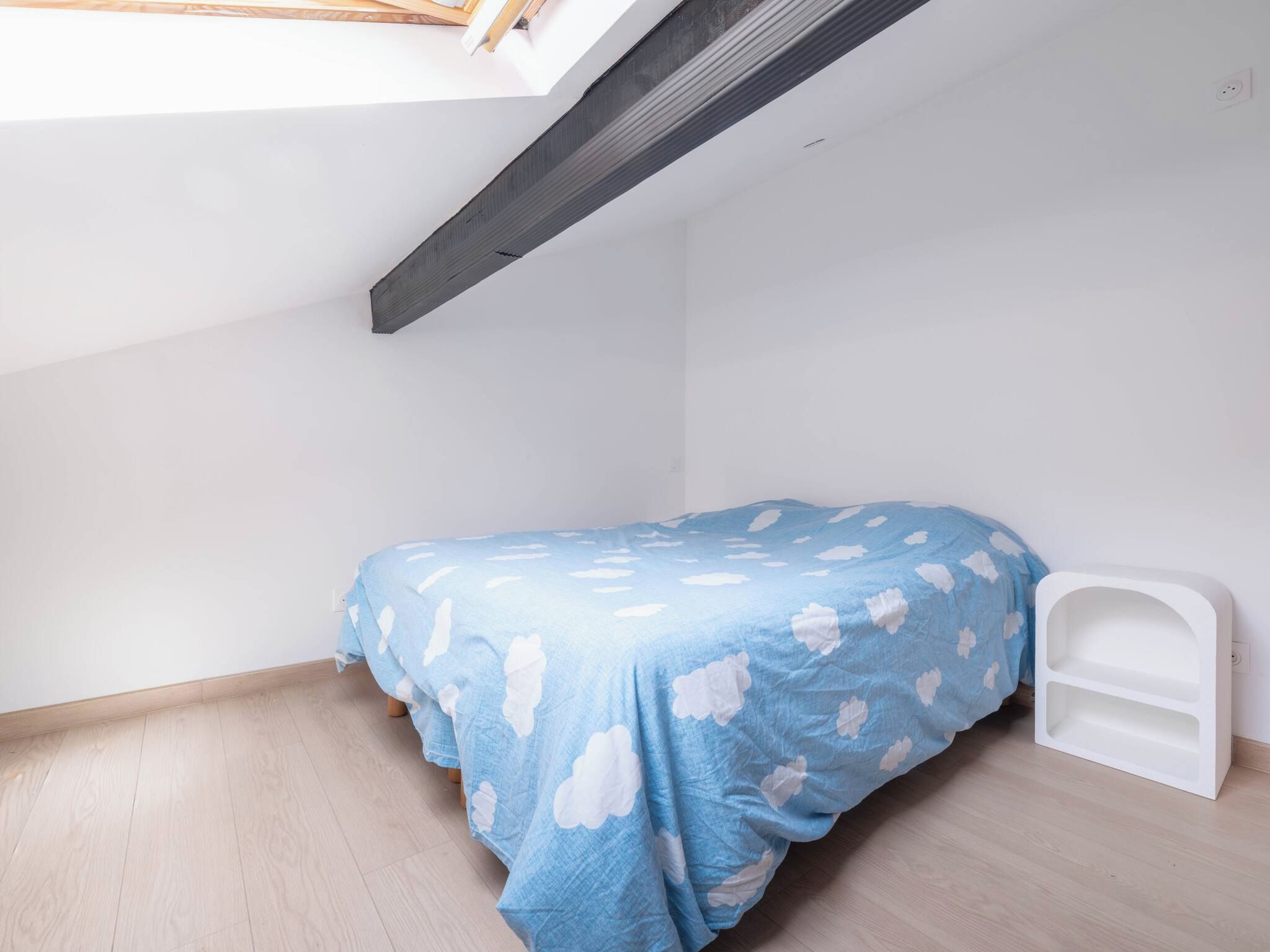 Een kleine kamer met een enkel bed, schuine wand, witte muur en houten vloer.